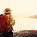 Bild einer Frau mit Trekking-Kleidung und mit grossem Rucksack, die in wunderschöner Natur auf einen See im Abendlicht schaut.