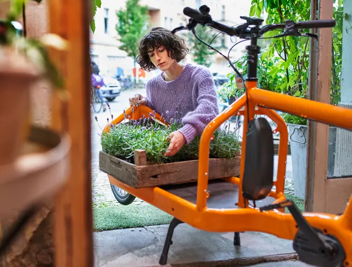 Junge Gärtnerin mit Blumenkiste, die sie auf ein Lastenvelo stellt - Sinnbild für die nachhaltige Anlagestrategie von Abendrot.