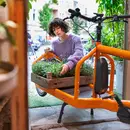 Junge Gärtnerin mit Blumenkiste, die sie auf ein Lastenvelo stellt - Sinnbild für die nachhaltige Anlagestrategie von Abendrot.