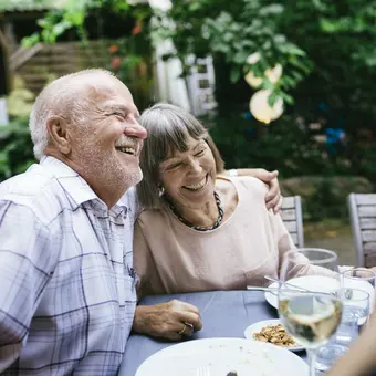 Bild eines Rentnerpaares, dass zusammen mit anderen Personen an einem Gartentisch sitzt und lachend diskutiert.